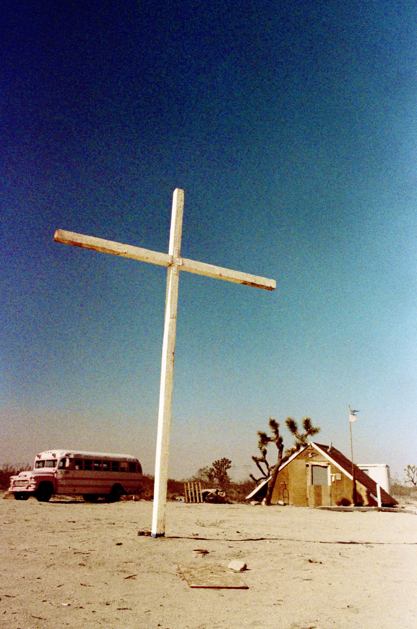 Wooden cross stands tall against a deep blue sky, Mojave landscape, by G. John Slagle.
