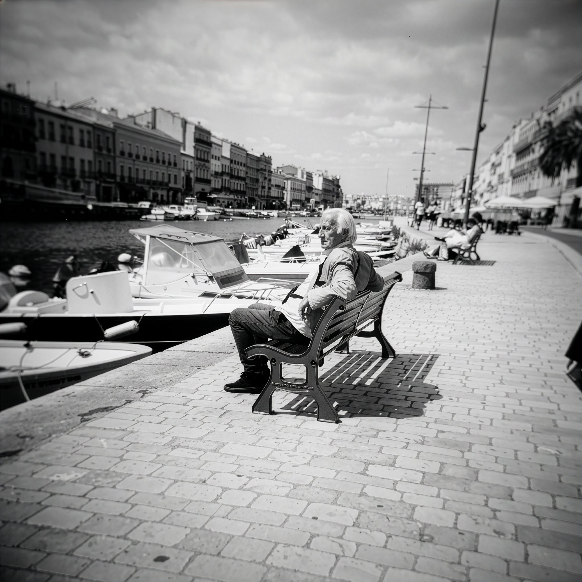 Older man on a bench beside boats moored along the harbor, S&egrave;te, France.